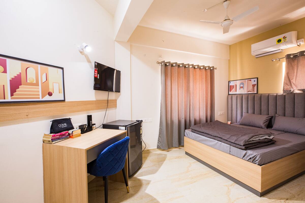 A bedroom with a bed, a desk, a chair, a TV, and an air conditioner.