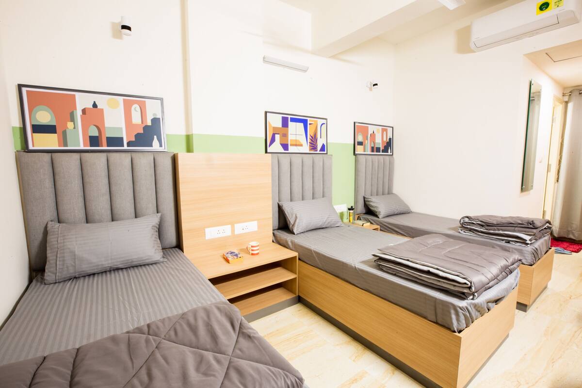 A modern hotel room with two single beds, a wooden headboard, a small table, and a wall-mounted air conditioner.