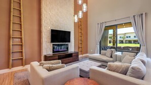 A modern living room with a flat-screen TV, beige sofas, a wooden coffee table, and a brick accent wall.