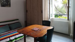 Une pièce avec une table en bois, un canapé agrémenté de coussins colorés, une armoire et une fenêtre donnant sur des arbres.