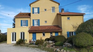 Un bâtiment à deux étages, avec une façade jaune, des volets bleus et une allée gravillonnée.