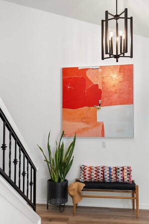 A staircase with a black railing, a wall-mounted abstract painting, a potted plant, and a bench with colorful cushions. - Designer Oasis minutes from Scottsdale Events - Heated Pool - Hot Tub - Sleeps 8 (Scottsdale)