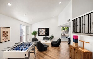 A modern room with a foosball table, comfortable seating, a chessboard, and a large window with blinds. - Designer Oasis minutes from Scottsdale Events - Heated Pool - Hot Tub - Sleeps 8 (Scottsdale)