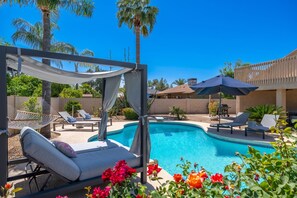 A pool area with lounge chairs, a hammock, and a pergola with a canopy.