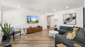 A modern living room with a grey sofa, a wooden coffee table, and a black bench. There is a wooden cabinet with decorative items and a painting of a desert landscape. - Designer Oasis minutes from Scottsdale Events - Heated Pool - Hot Tub - Sleeps 8 (Scottsdale)
