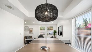 A modern room with a ping pong table, a large woven pendant light, and a view of the outdoors through large windows. - Designer Oasis minutes from Scottsdale Events - Heated Pool - Hot Tub - Sleeps 8 (Scottsdale)
