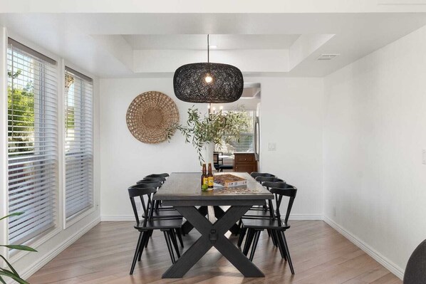 A dining area with a rectangular table, black chairs, a woven wall hanging, and a hanging light fixture.