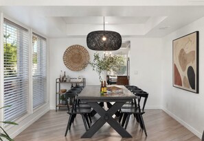 A dining area with a long table, black chairs, a woven wall hanging, and a pendant light. - Designer Oasis minutes from Scottsdale Events - Heated Pool - Hot Tub - Sleeps 8 (Scottsdale)