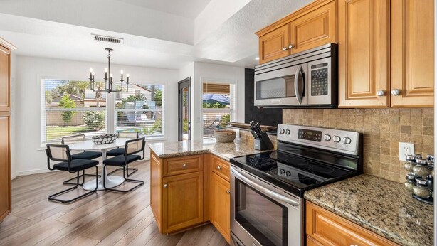 A modern kitchen with wooden cabinets, a granite countertop, stainless steel appliances, and a dining area with a view of the backyard. - Designer Oasis minutes from Scottsdale Events - Heated Pool - Hot Tub - Sleeps 8 (Scottsdale)