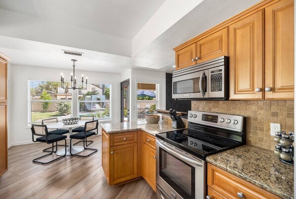 A modern kitchen with wooden cabinets, a granite countertop, stainless steel appliances, and a dining area with a view of the backyard. - Designer Oasis minutes from Scottsdale Events - Heated Pool - Hot Tub - Sleeps 8 (Scottsdale)