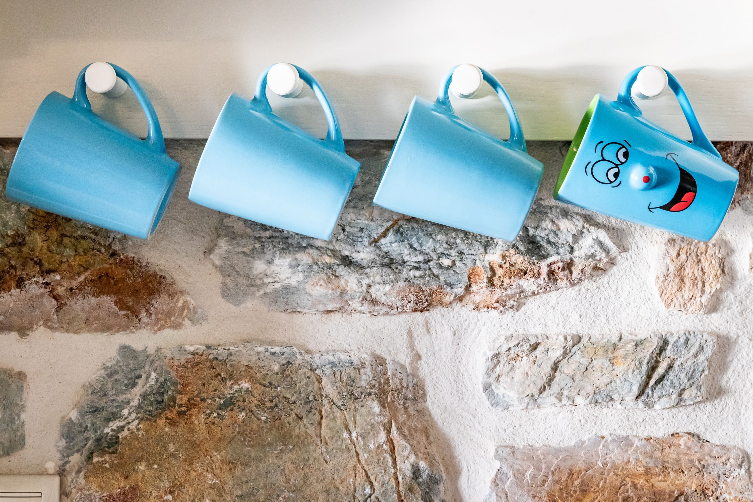 Four blue mugs with handles on a stone wall.