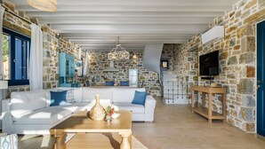 A spacious living area with a stone wall, a white sofa, a wooden coffee table, and a television mounted on the wall.