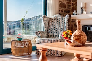 Un salon chaleureux avec un fauteuil à motifs, une table en bois et une petite table d’appoint en osier sur laquelle se trouve un panier de fruits.
