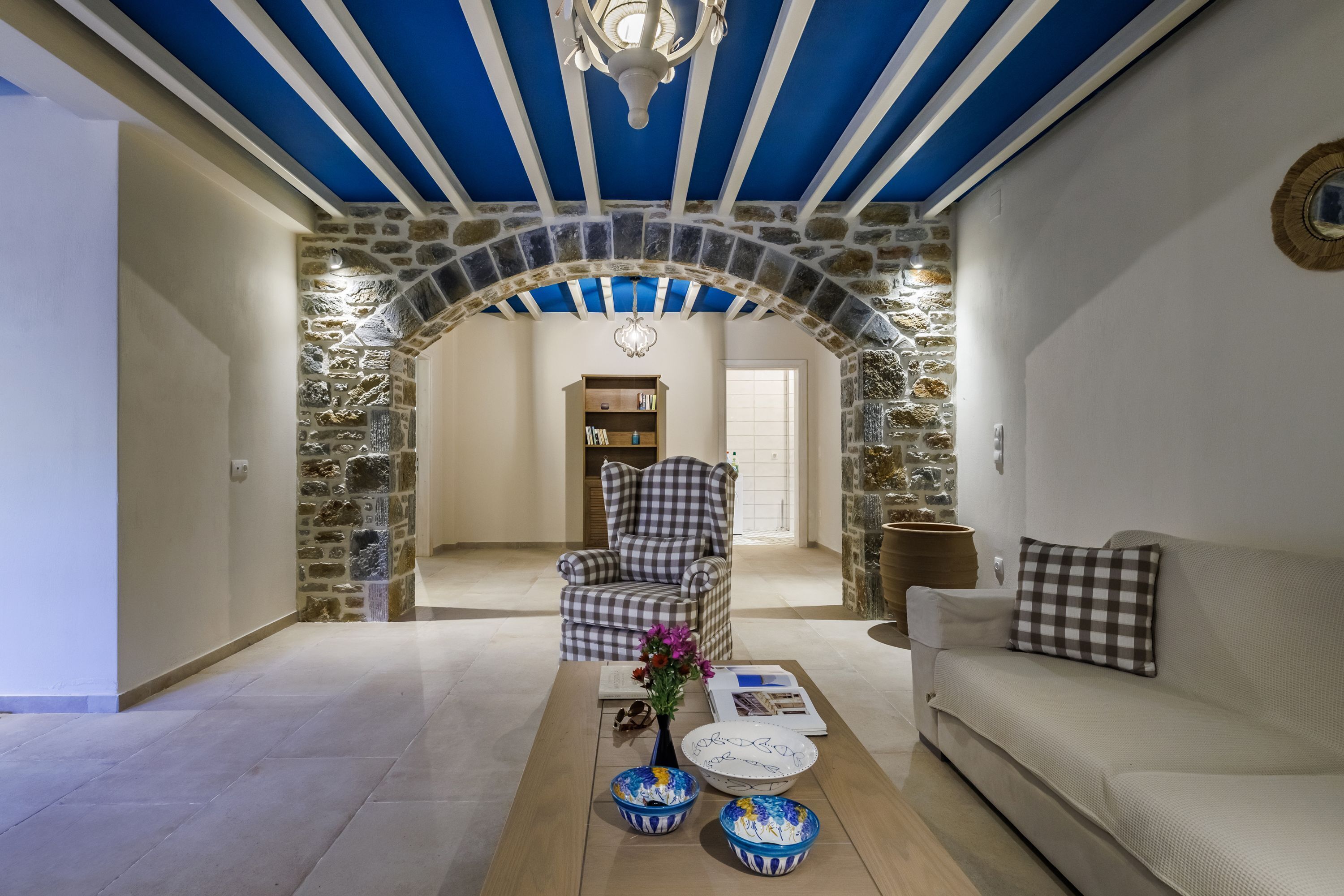 A living room with a stone archway, a checkered armchair, a sofa, and a coffee table with decorative bowls.