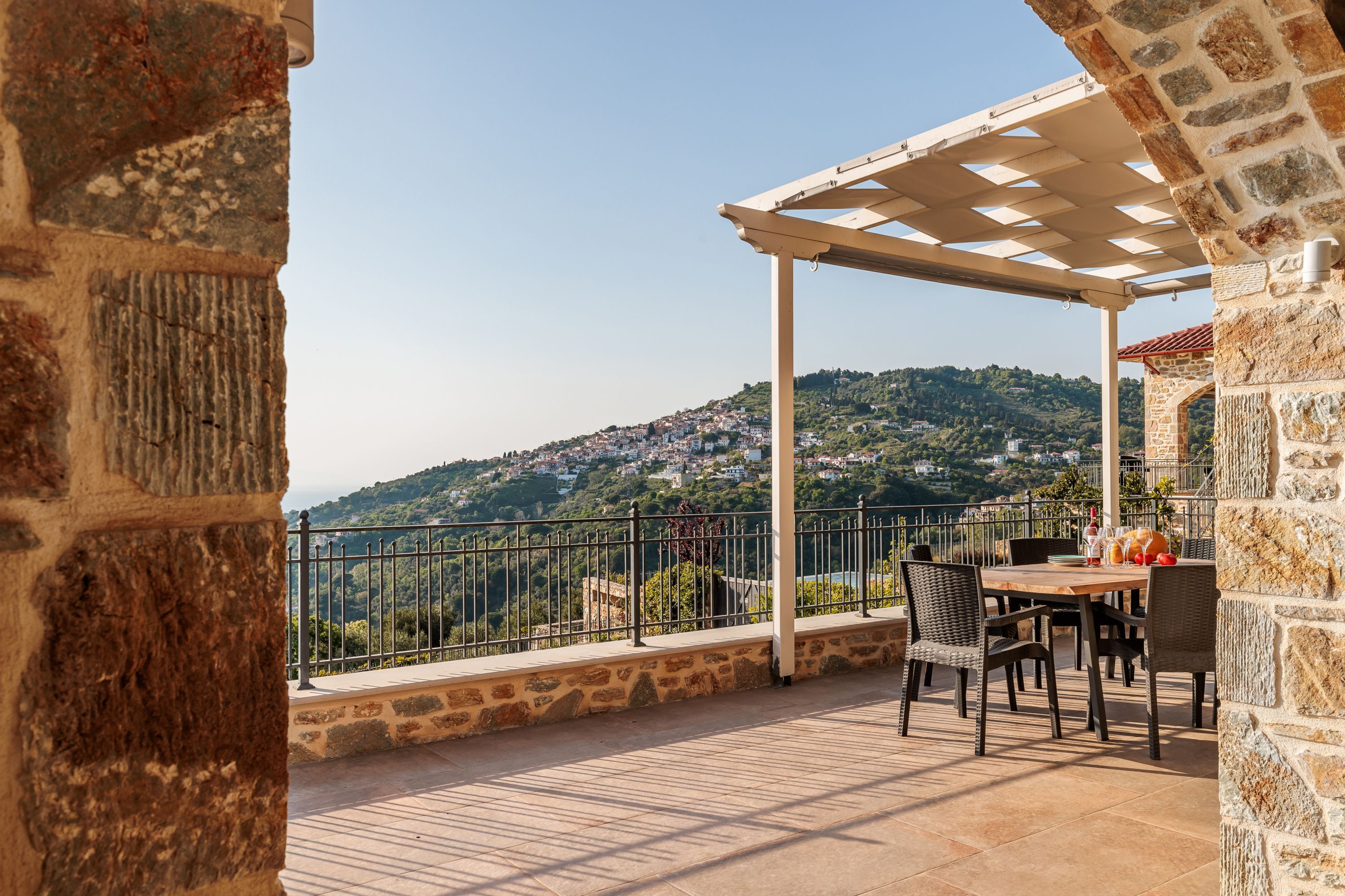 A terrace with stone walls, a pergola, and a table with chairs.