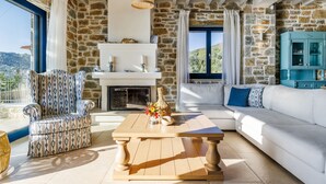 A living room with a stone wall, a white sofa, a patterned armchair, a wooden coffee table, and a fireplace.