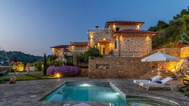 A stone villa with a swimming pool and lounge chairs.