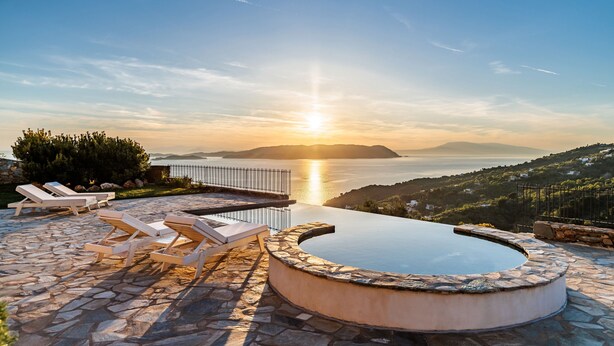 Ein Pool mit Liegestühlen, einer Steinterrasse und Blick auf Meer und Hügel.
