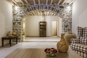 Un arc en pierre mène à une pièce dotée d’un plancher en bois, d’une bibliothèque et d’un canapé à motifs à carreaux.