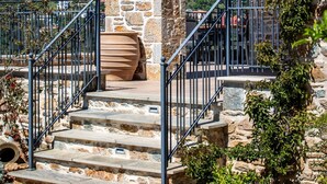 Ein Steinhaus mit einer Treppe, die zu einem überdachten Bereich führt, umgeben von Grünpflanzen.