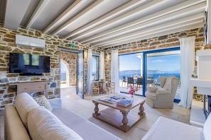 A stone-walled room with a television, a sofa, a coffee table, and a patterned armchair.