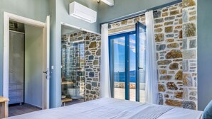 Ein Schlafzimmer mit einer Steinwand, einer Glastür, die auf einen Balkon führt, und einem Bett mit weißer Bettdecke.