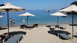 Ein Strand mit Liegestühlen und Sonnenschirmen, ein klares blaues Meer und Boote in der Ferne.