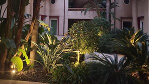 A courtyard with a two-story building, surrounded by tropical plants and palm trees. - Appartement Dans une Résidence ART Deco!! au Bord de la Plage (La Ciotat)