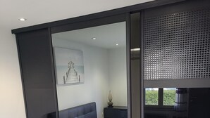 A modern bedroom with a large bed, a sliding door closet, and a window with a view of greenery. - Appartement Dans une Résidence ART Deco!! au Bord de la Plage (La Ciotat)