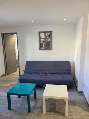 Uma sala de estar com um sofá azul escuro, uma mesa de centro verde água e uma mesa lateral branca.