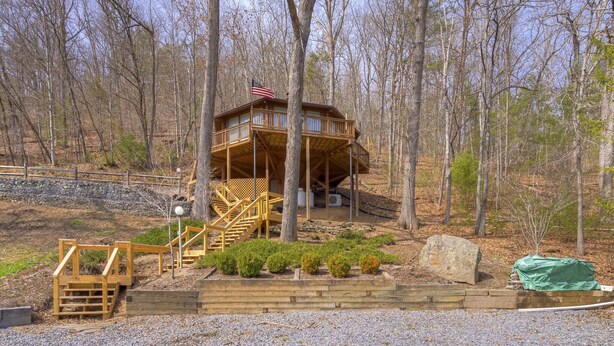 A wooden cabin with a balcony, surrounded by trees and a gravel path. - Cozy rental near Greenbrier Resort with a deck, stunning views modern-rustic charm, and full kitchen (White Sulphur Springs)