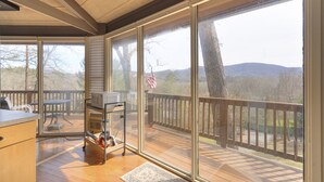A spacious deck with a wooden floor, a table, and a grill cart. - Cozy rental near Greenbrier Resort with a deck, stunning views modern-rustic charm, and full kitchen (White Sulphur Springs)