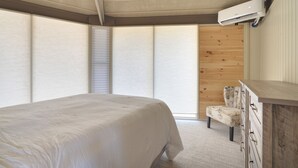 A bedroom with a bed, a chair, a dresser, and a window with blinds. - Cozy rental near Greenbrier Resort with a deck, stunning views modern-rustic charm, and full kitchen (White Sulphur Springs)