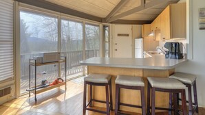 A kitchen with a large island, bar stools, and a view of a deck. - Cozy rental near Greenbrier Resort with a deck, stunning views modern-rustic charm, and full kitchen (White Sulphur Springs)