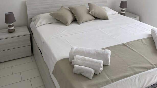 A neatly made bed with a beige bedspread, two pillows, and a set of towels on the side. - Daisy Apartment (Piano di Sorrento)