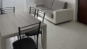 A modern living room with a dining table and chairs, a sofa, and a hanging light fixture. - Daisy Apartment (Piano di Sorrento)