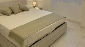 A bedroom with a bed, a nightstand, a lamp, and a window with sheer curtains. - Daisy Apartment (Piano di Sorrento)