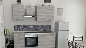 A modern kitchen with a built-in oven, a refrigerator, and a dining area with a table and chairs. - Daisy Apartment (Piano di Sorrento)