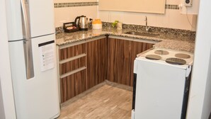 A compact kitchen with a refrigerator, stove, and wooden cabinets.
