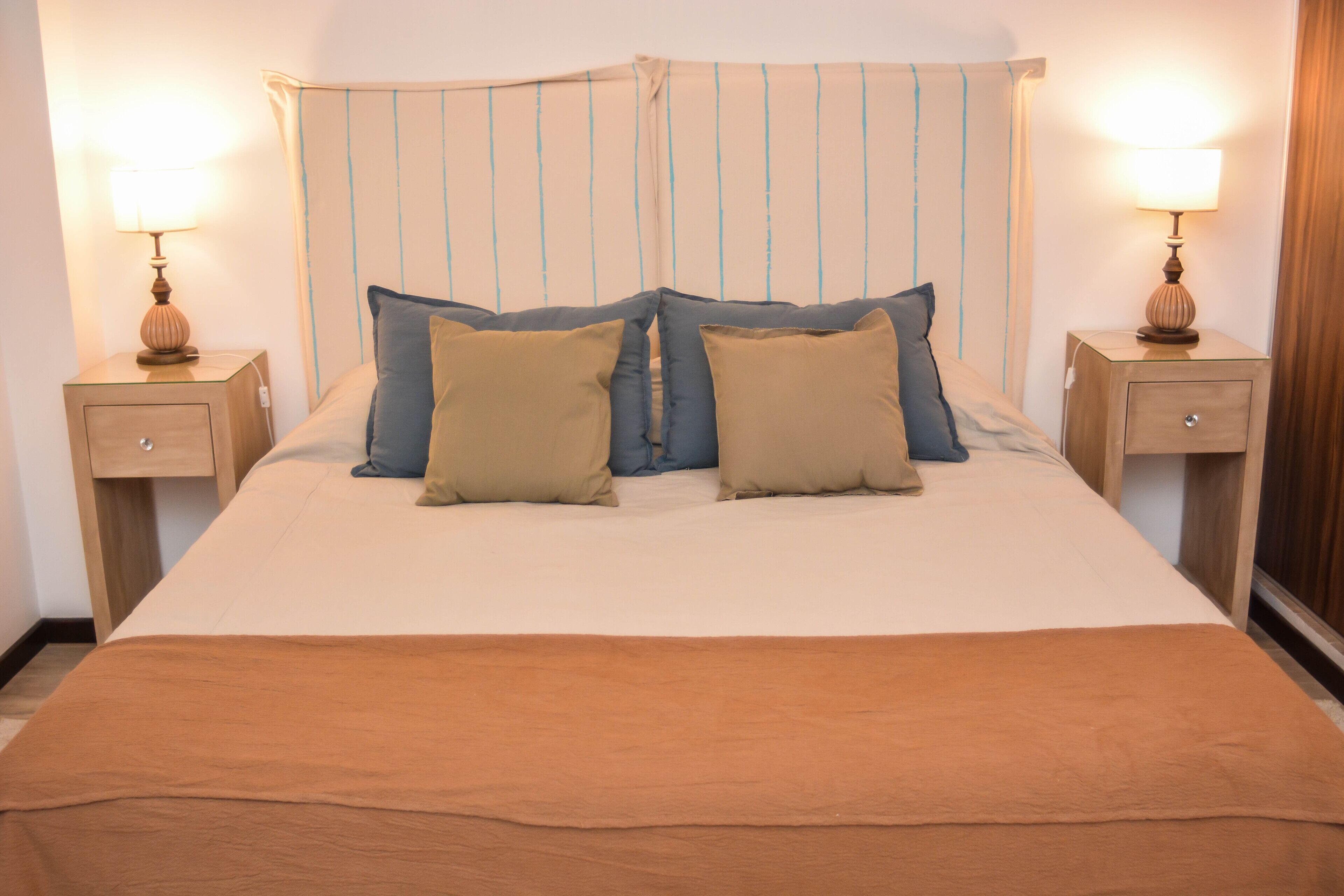 A neatly made bed with two pillows, a brown blanket, and two bedside tables with lamps.