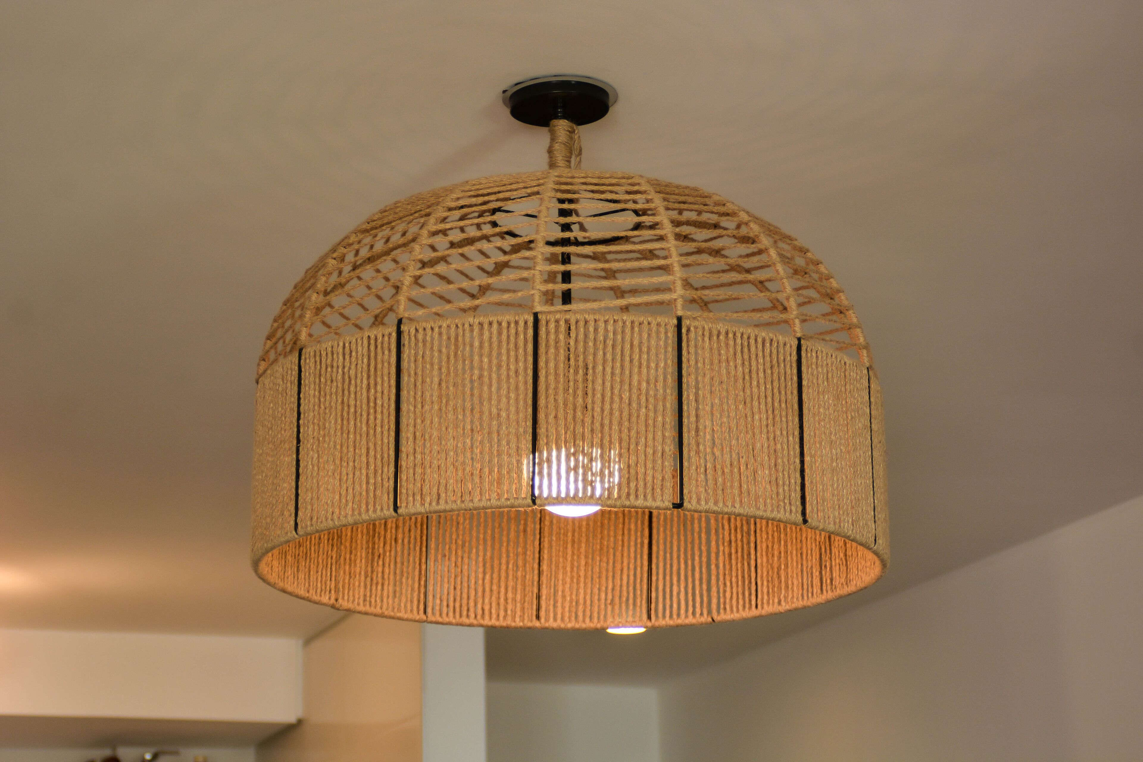 Un luminaire suspendu en forme de dôme, fabriqué à partir de fibres tressées, avec une ampoule centrale, et fixé au plafond.