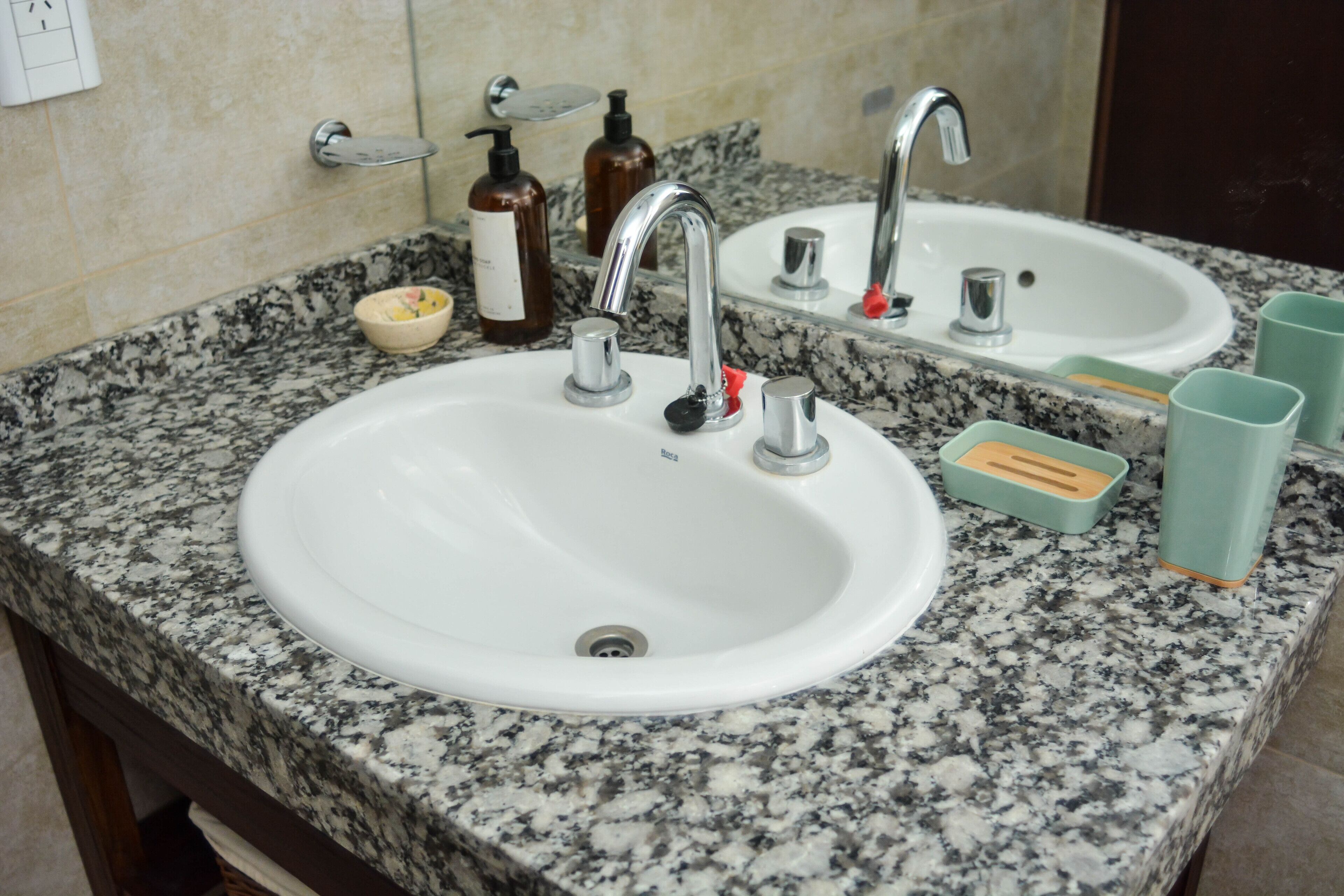 A bathroom with a granite countertop, a white sink, a mirror, and toiletries.