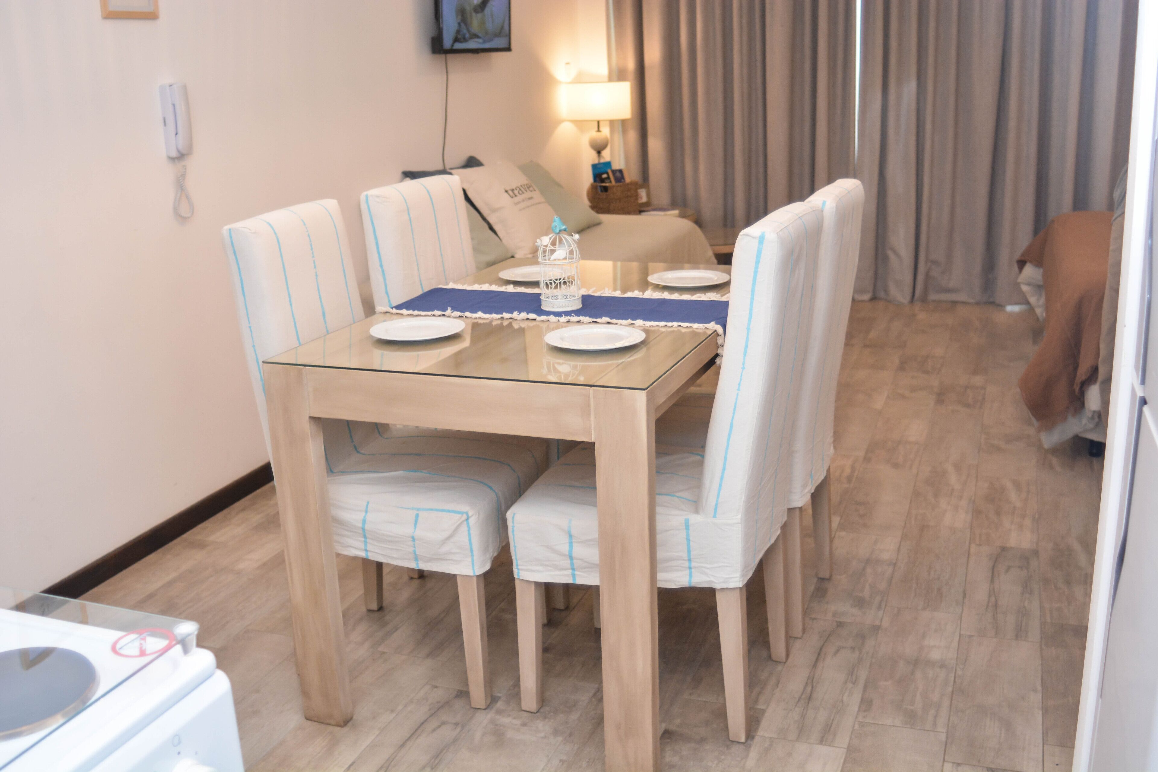 A dining area with a glass-top table, four chairs, a placemat, and a decorative lantern.