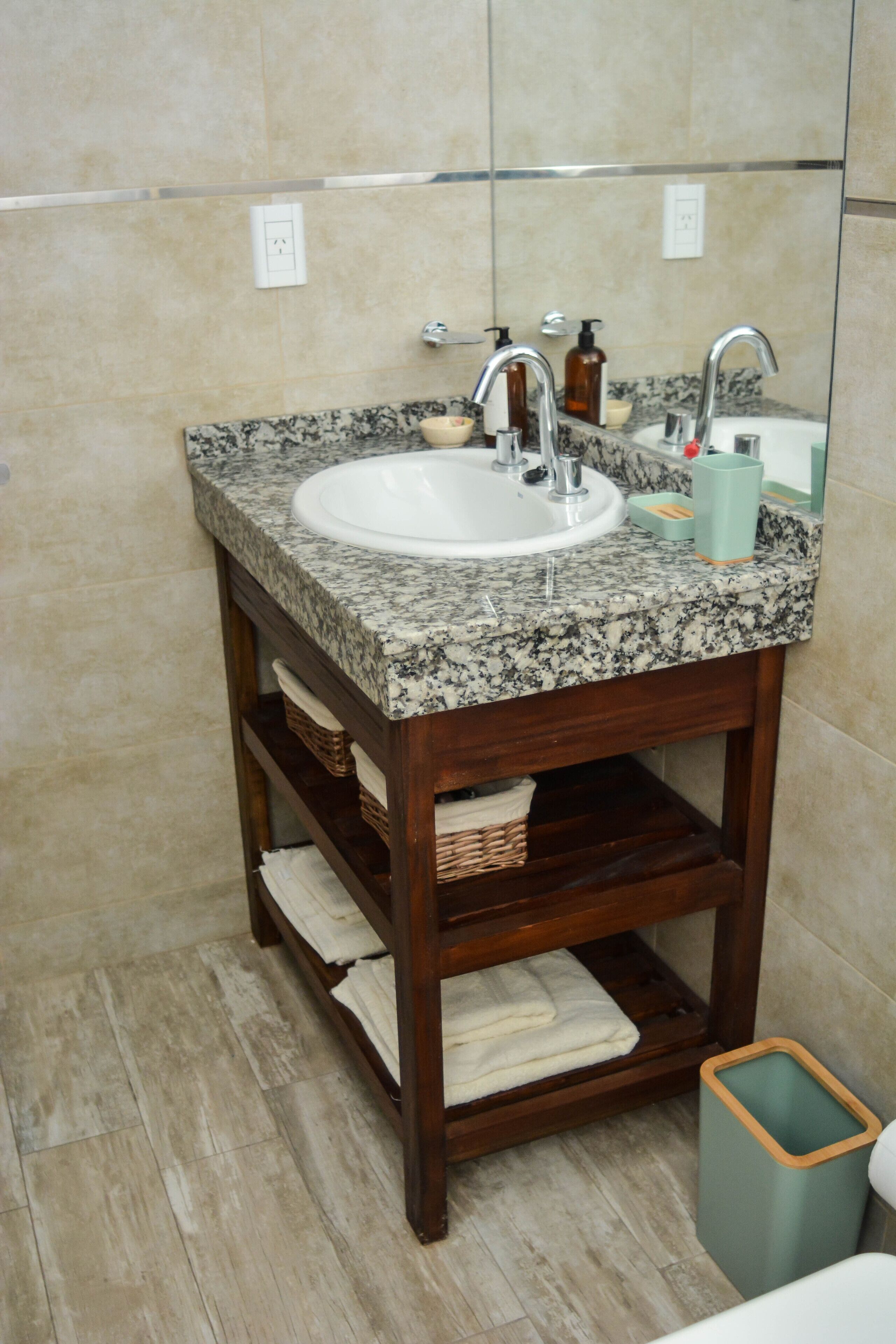 Un baño con lavamanos de encimera de granito, tocador de madera y espejo arriba.
