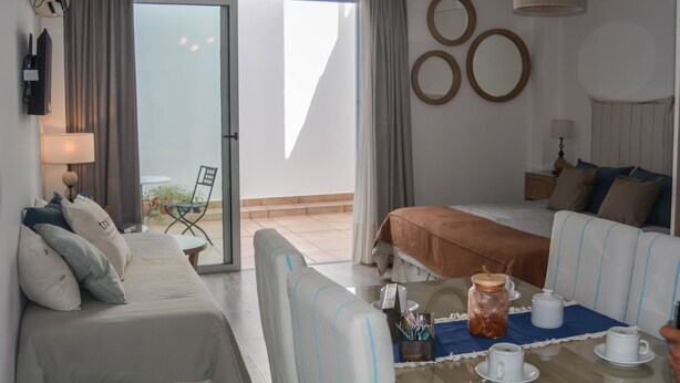A hotel room with a bed, a sofa, a dining table with cups and a jar, and a view of the outdoors.