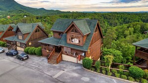 A row of log cabins with steep roofs, surrounded by lush greenery and mountains in the background. - Near Pigeon Forge | Theater, Game Room, Hot Tub & Resort Pools (Sevierville)