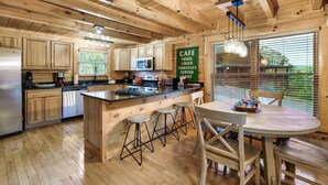 A wooden cabin-style kitchen with a central island, bar stools, and a dining table. - Near Pigeon Forge | Theater, Game Room, Hot Tub & Resort Pools (Sevierville)