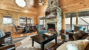 A cozy log cabin interior with a stone fireplace, wooden walls, and a dining area. - Near Pigeon Forge | Theater, Game Room, Hot Tub & Resort Pools (Sevierville)