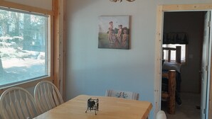 Ein Essbereich mit Holztisch und Stühlen, einer Kandelaberleuchte, einem Bild an der Wand und Blick durch ein Fenster.