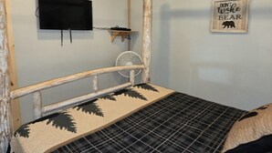 Ein Etagenbett mit Fernseher und Ventilator, ein motivierendes Zitat an der Wand und eine Bettdecke mit Karomuster.
